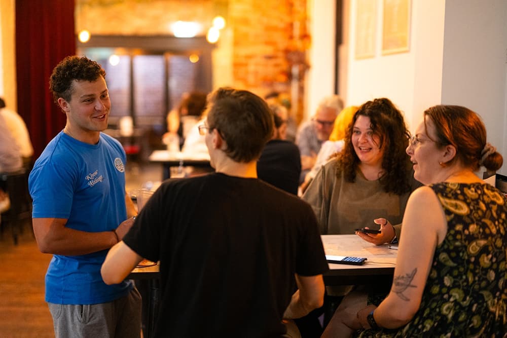 A Know Brainer Trivia host smiling and talking with a team at their table.